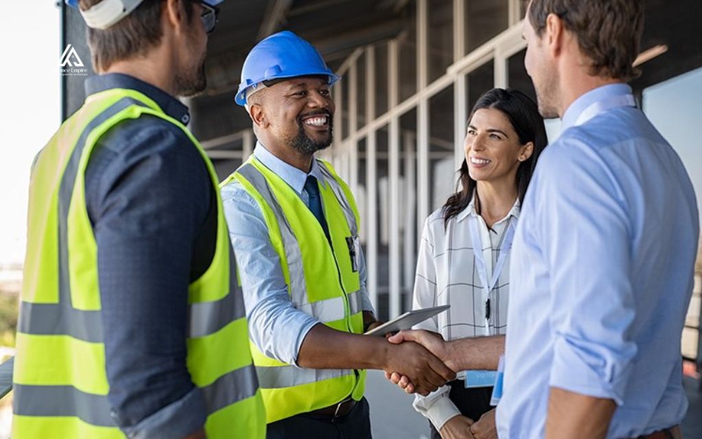 Project team members in safety vests and hard hats shake hands and smile during a conversation on a construction site